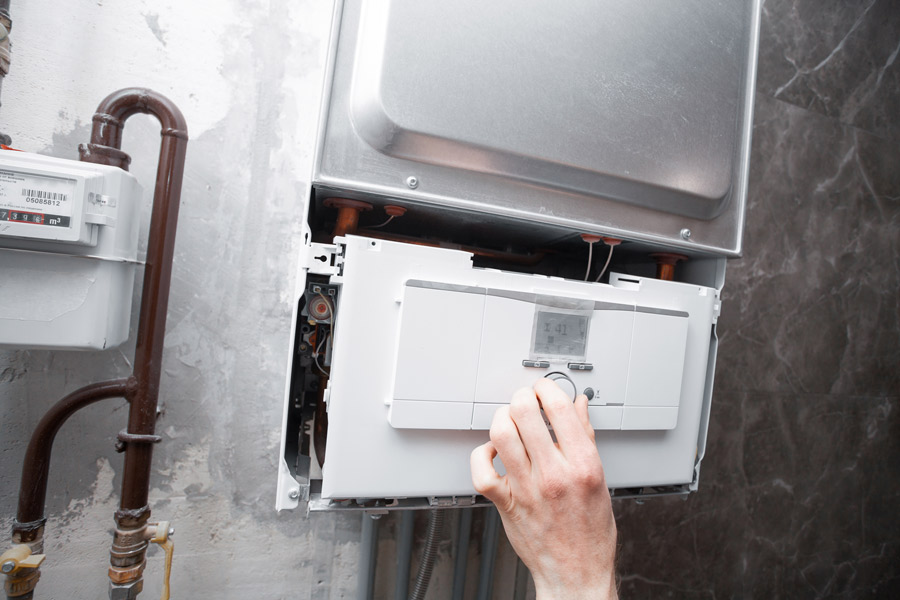 Furnace and heating services- Someone turning a nozzle on a white heating system installed into the wall.